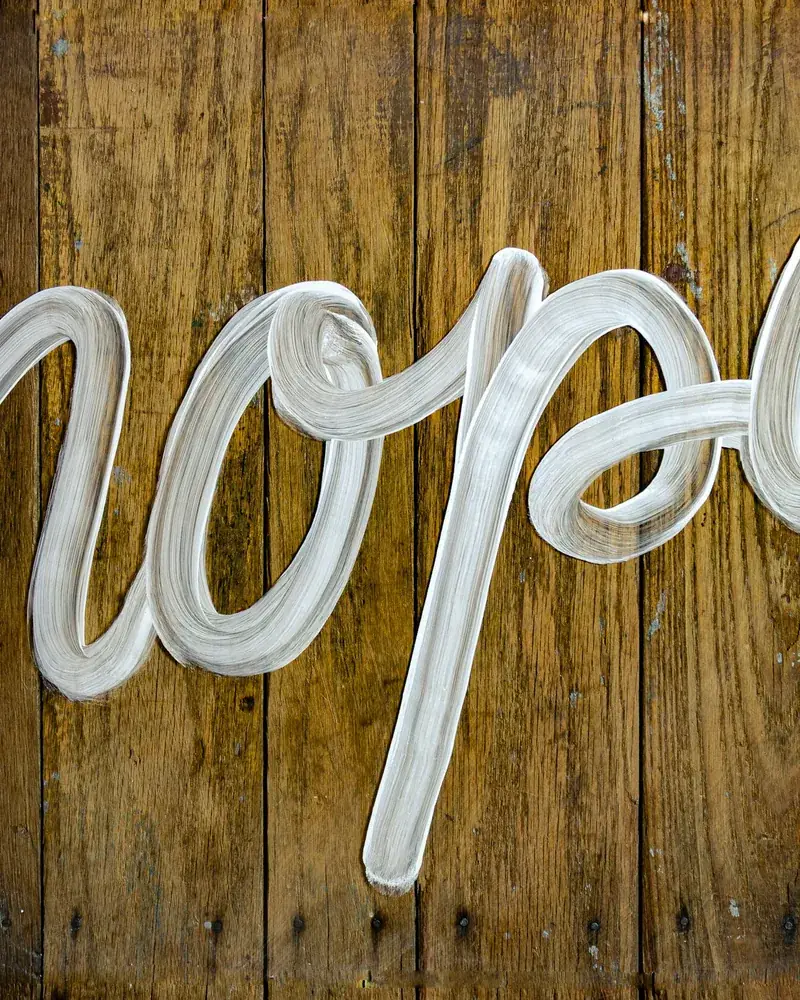 Letras pintadas a mano sobre un panel de madera y cristal, con perfiles definidos